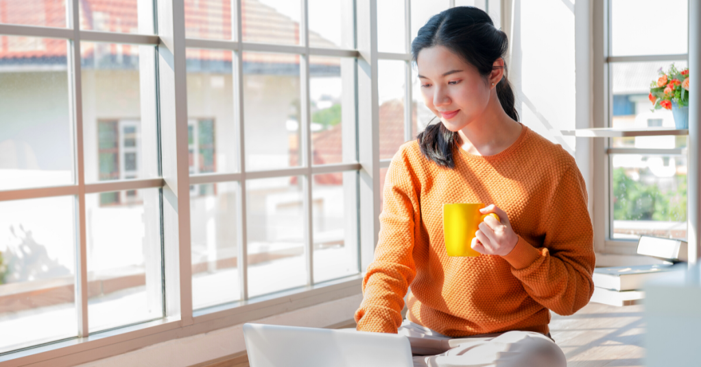 young asian woman on computer holding yellow coffee cup